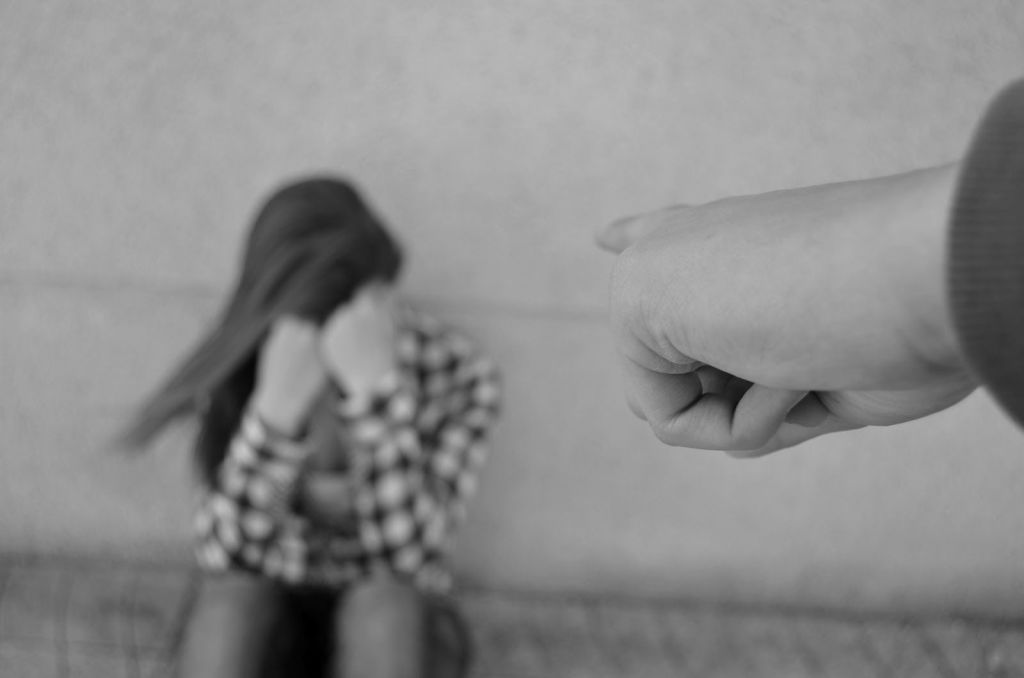 Chica sentada en el suelo tapando su cara con sus manos mientras una persona le apunta con el dedo