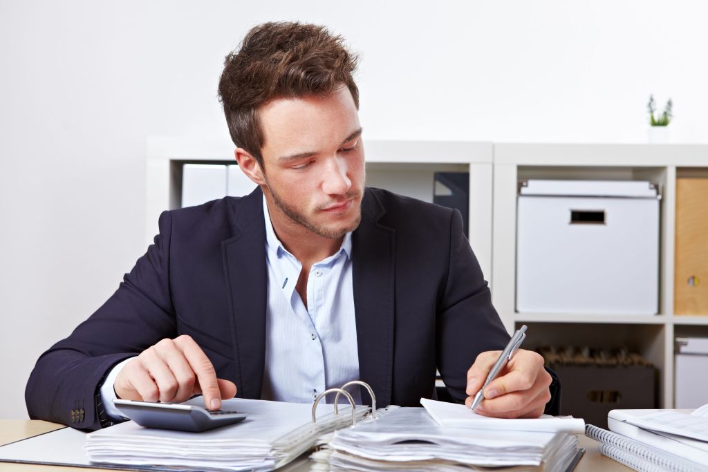 Hombre de negocios firmando unos papeles en su oficina y calculando con una calculadora