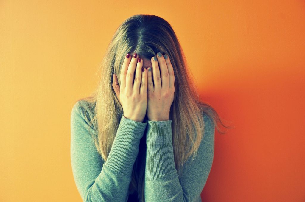 Mujer con las manos en la cara estresada apoyada en una pared naranja