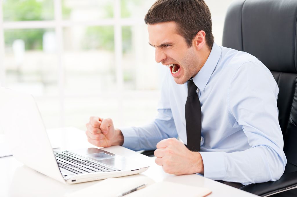 Un hombre con traje gritando con cara de satisfacción frente a su portátil