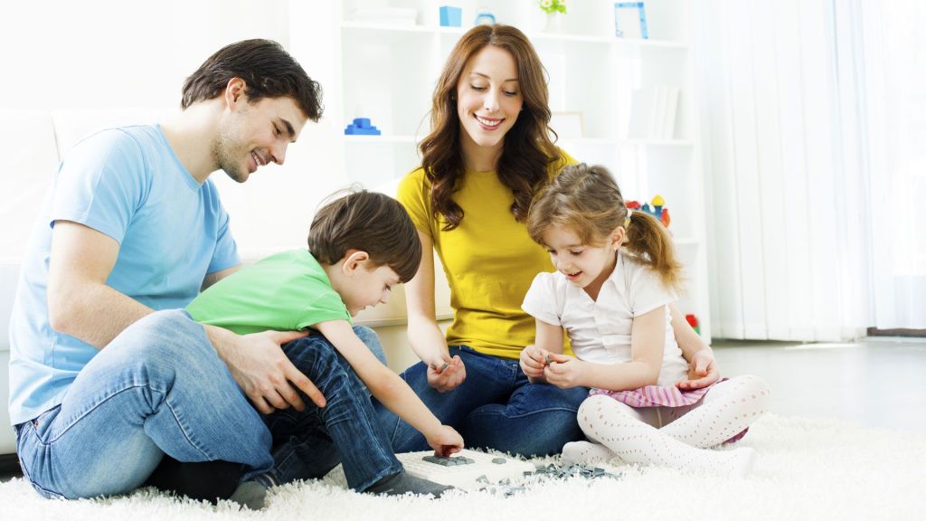 Un padre y una madre jugando con sus dos hijos en el suelo de su salon