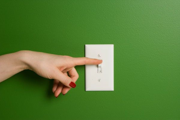 Mano apagando un interruptor de la luz blanco sobre una pared verde
