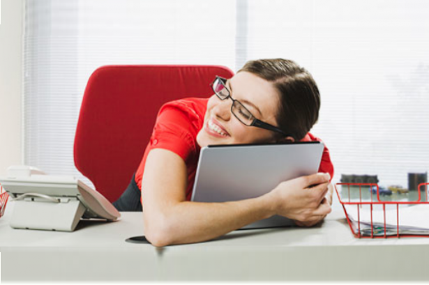 Mujer con gafas sentada en la mesa de su oficina abrazando a su portatil