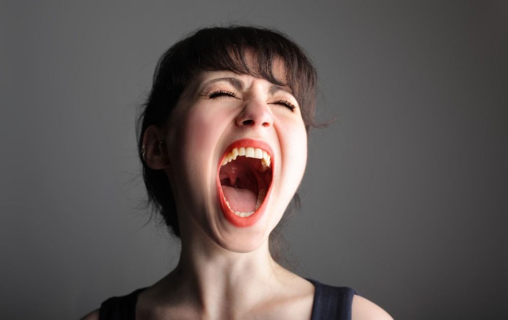 Mujer gritando con la boca abierta sobre un fondo gris negruzco