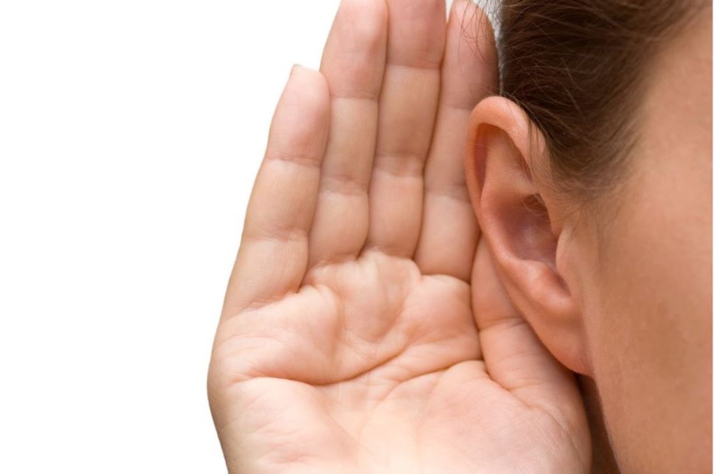 Mujer poniendo su mano en su oido haciendo el gesto de escuchar