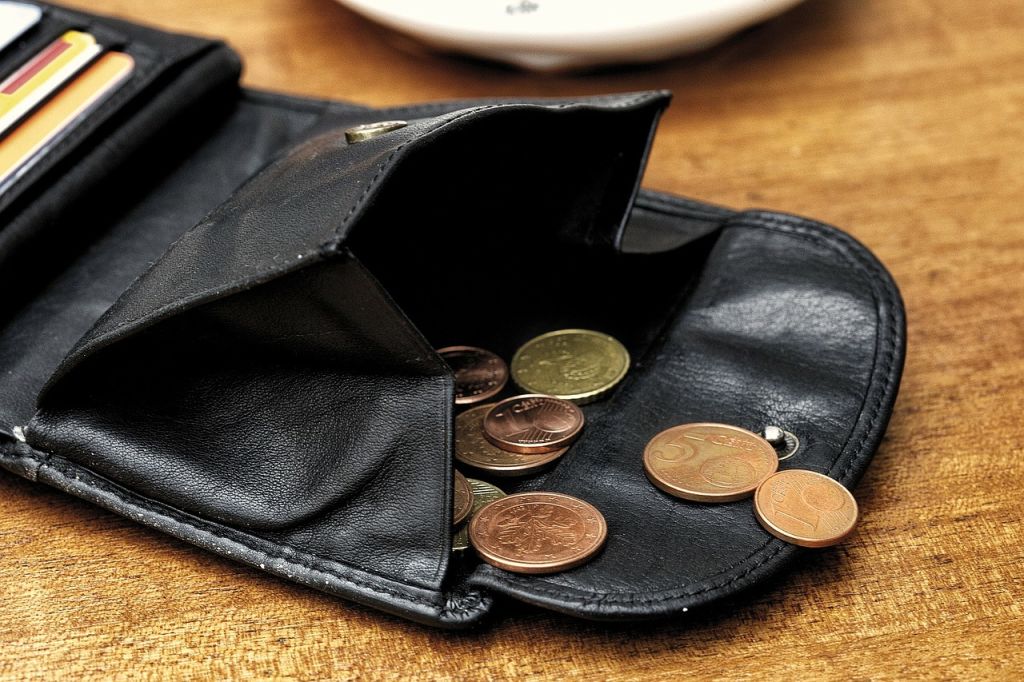 Una billetera abierta encima de una mesa de la que salen varias monedas de centimos de euro
