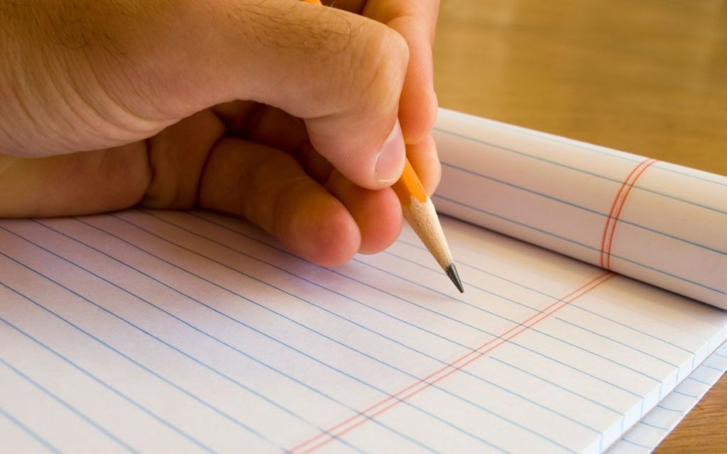 Mano de un hombre con un lapiz escribiendo en un cuaderno a rayas