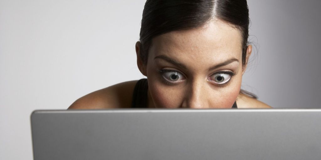 Mujer sorprendida con los ojos muy abiertos mirando a la pantalla de su computadora