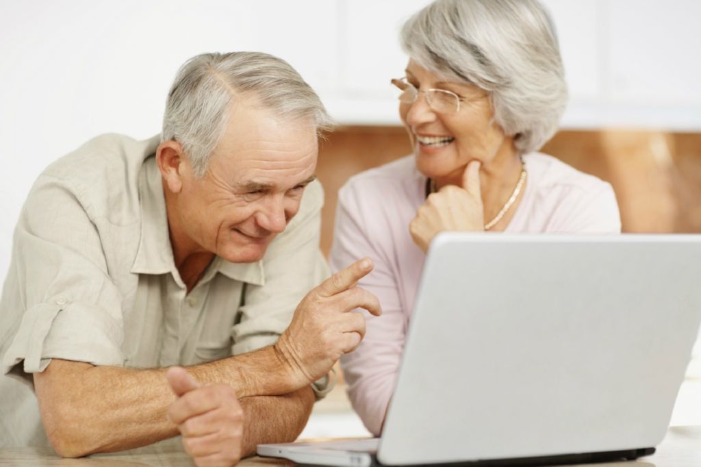 Dos personas ancianas riendo felices enfrente de un ordenador portatil
