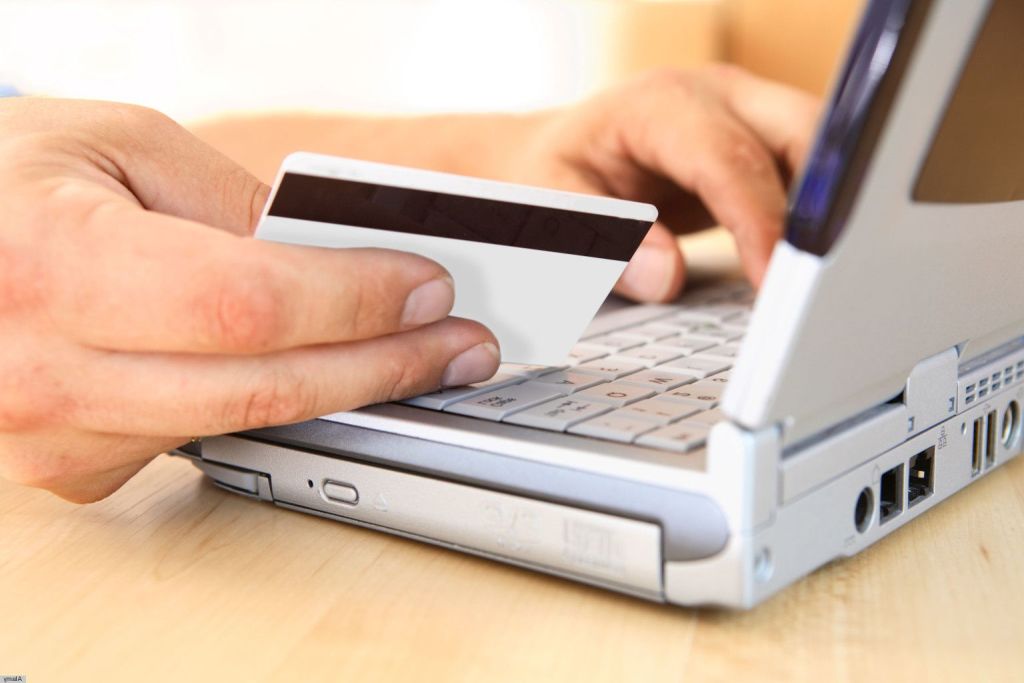 Una persona sosteniendo una tarjeta de crédito en su mano enfrente de un portatil para hacer una compra online