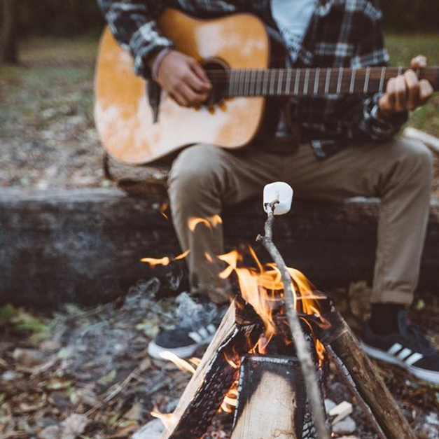 Dos personas acampando mientras uno toca la guitarra