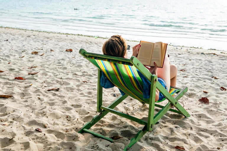 Mujer sentada en la playa leyendo un libro