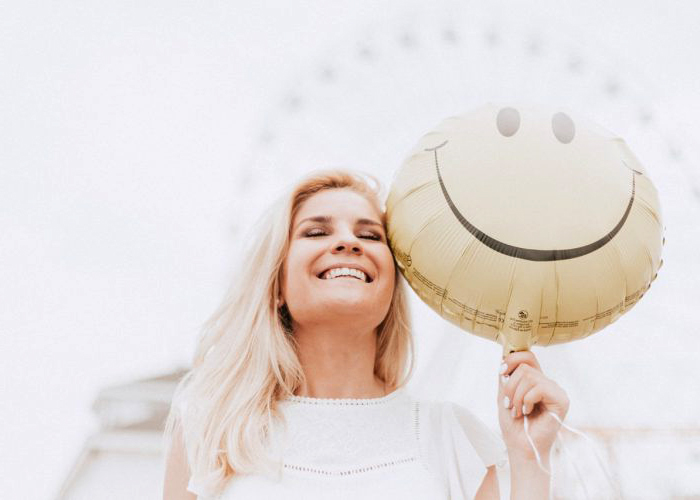 Mujer sonriendo mientras sostiene globo de carita feliz