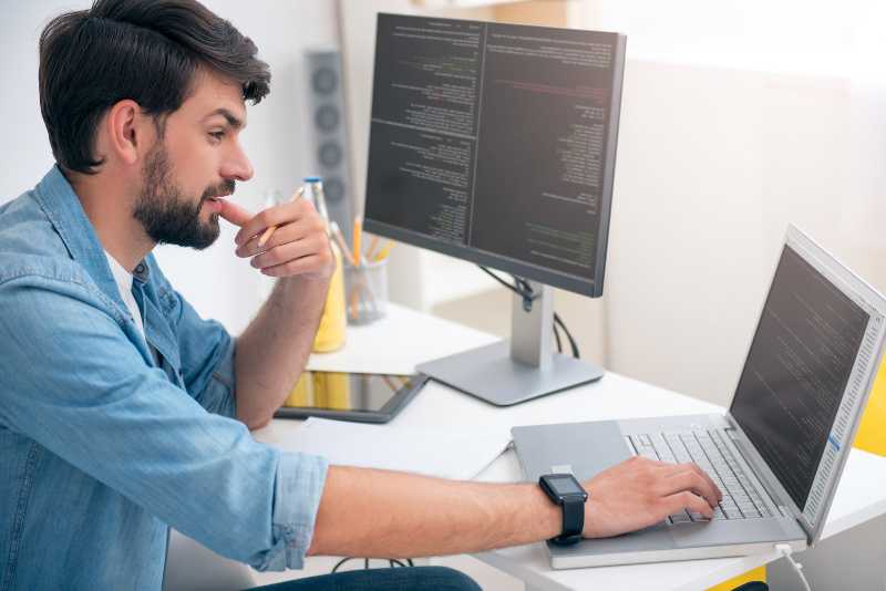 hombre mirando su computadora con la mano en al barbilla