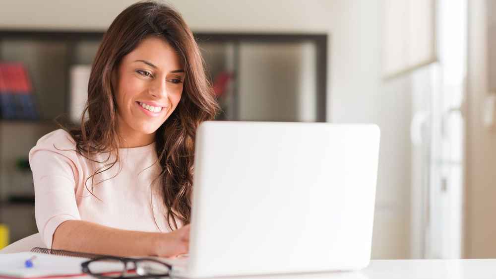 Mujer escribiendo en su portátil mientras sonríe