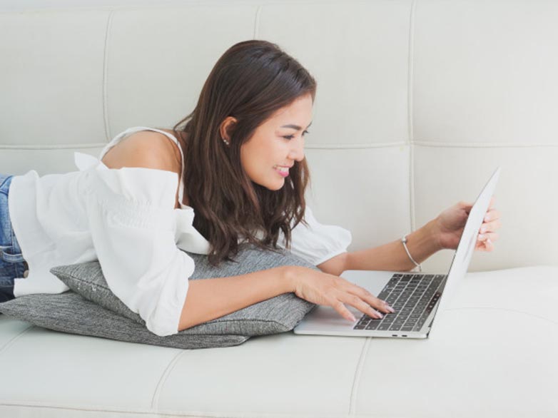 Mujer usando computadora acostada en un sofá