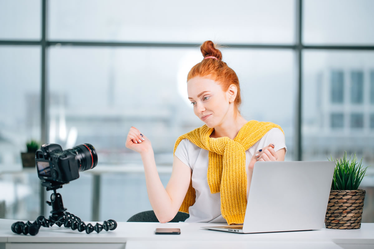 Mujer grabándose con una cámara sentada en un escritorio